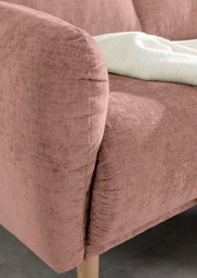 Nahaufnahme einer rosafarbenen Sofaecke mit weicher Textur und Holzfuß, von der Seite betrachtet.