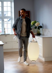 Mann in einer modernen Küche trägt eine leuchtende Akku-Leuchte mit Lautsprecher, seitliche Perspektive.