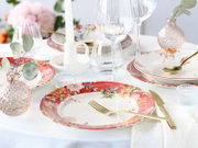 Festlich gedeckter Tisch mit floralem Porzellan-Geschirr mit rotem Rand, goldfarbenem Besteck, Wein- und Wassergläsern, Kerze und Deko in Pastelltönen, fotografiert in leichter Schrägansicht von vorne/oben