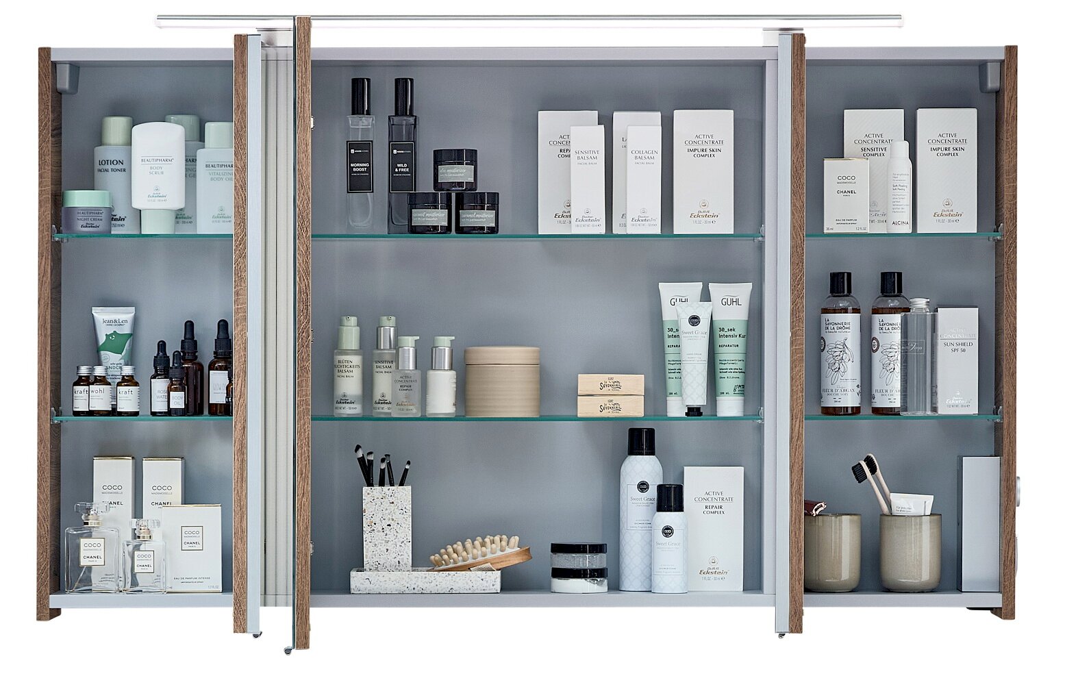 Badezimmerschrank mit drei Spiegeltüren, offenen Regalfächern und Glasböden in Holzoptik, gefüllt mit Kosmetik- und Pflegeprodukten; Frontansicht.