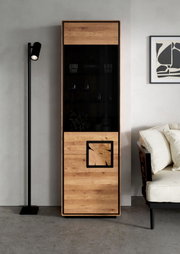 Hoher, schmaler Vitrinenschrank aus Holz mit schwarzer Glasfront und dekorativem Holzeinsatz, frontal in einem modernen Wohnzimmer inszeniert.