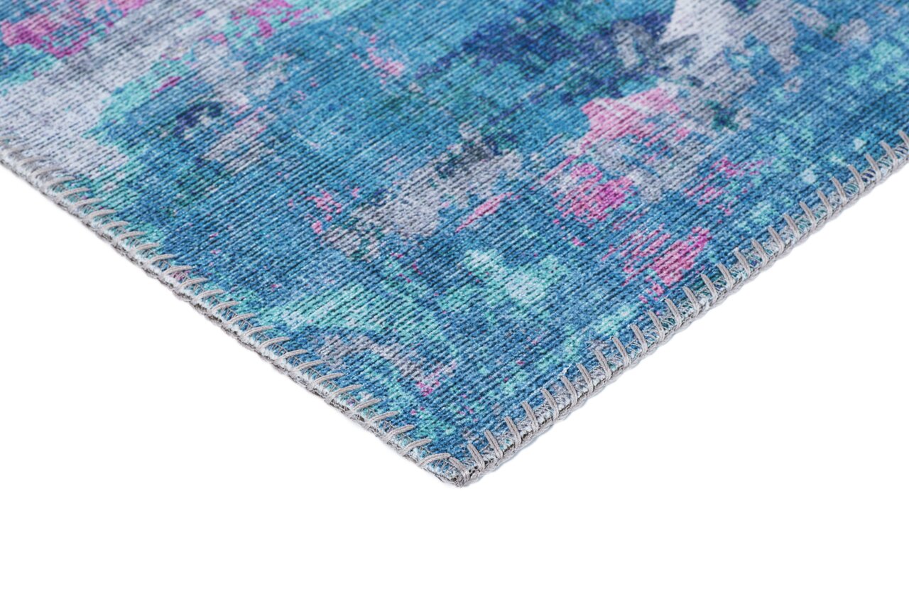 Nahaufnahme einer Ecke eines blauen Teppichs mit abstraktem Muster in Blau- und Pinktönen, von der Seite fotografiert.