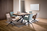 Modernes Esszimmer-Set mit großem Esstisch aus Holz und schwarzem X-Gestell, umgeben von gepolsterten Drehstühlen in Mintgrün und Beige; Perspektive: schräg von vorne auf Tisch und Stühle.