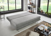 Graues Funktionssofa in flacher Position, seitliche Perspektive, in modernem Wohnzimmer mit großen Fenstern und stilvoller Dekoration.