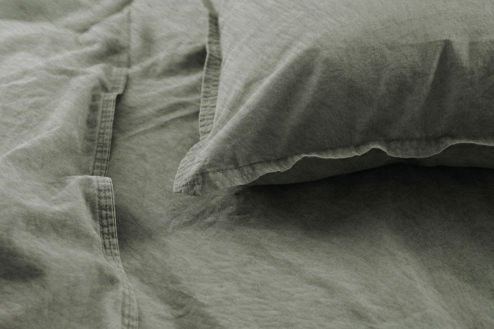 Nahaufnahme von olivgrüner Bettwäsche mit Kissenbezug, aus der Vogelperspektive fotografiert.