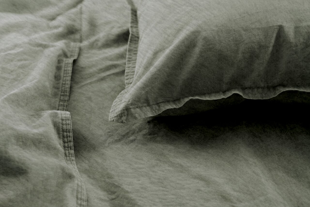 Nahaufnahme von olivgrüner Bettwäsche mit Kissenbezug, aus der Vogelperspektive fotografiert.