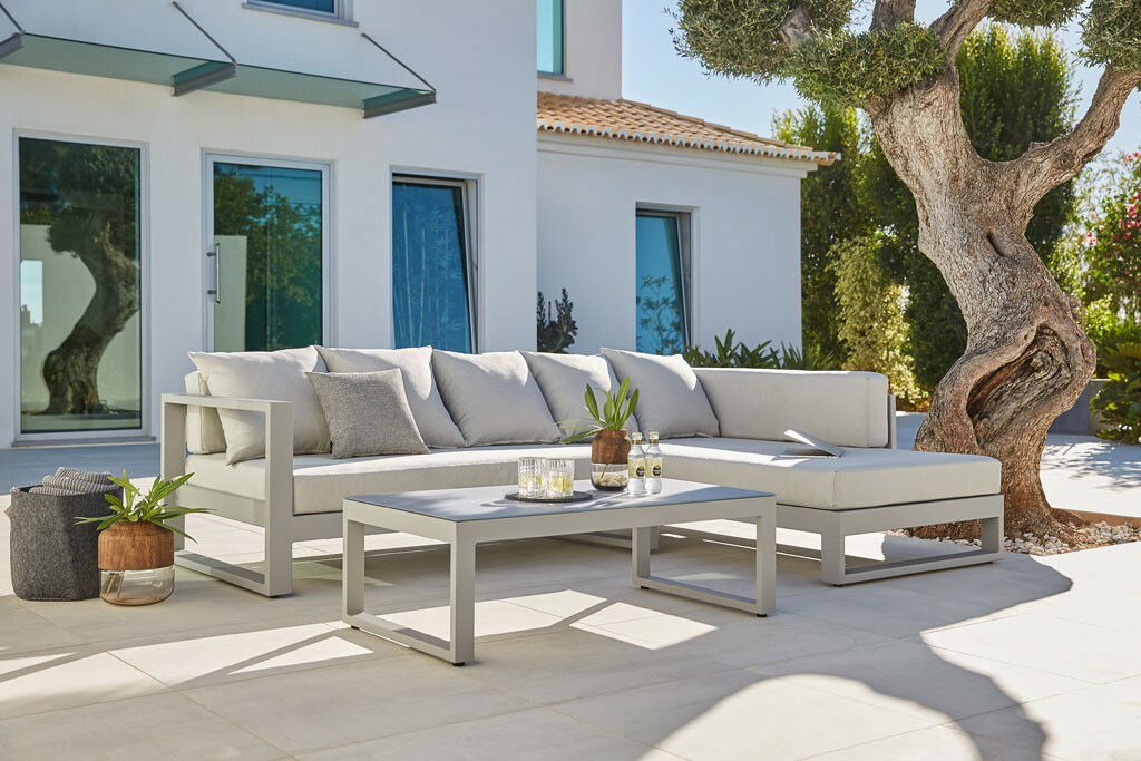 Modernes Lounge-Set in einem sonnigen Garten mit Blick auf ein stilvolles Sofa und einen Couchtisch, umgeben von Pflanzen und einem Baum.