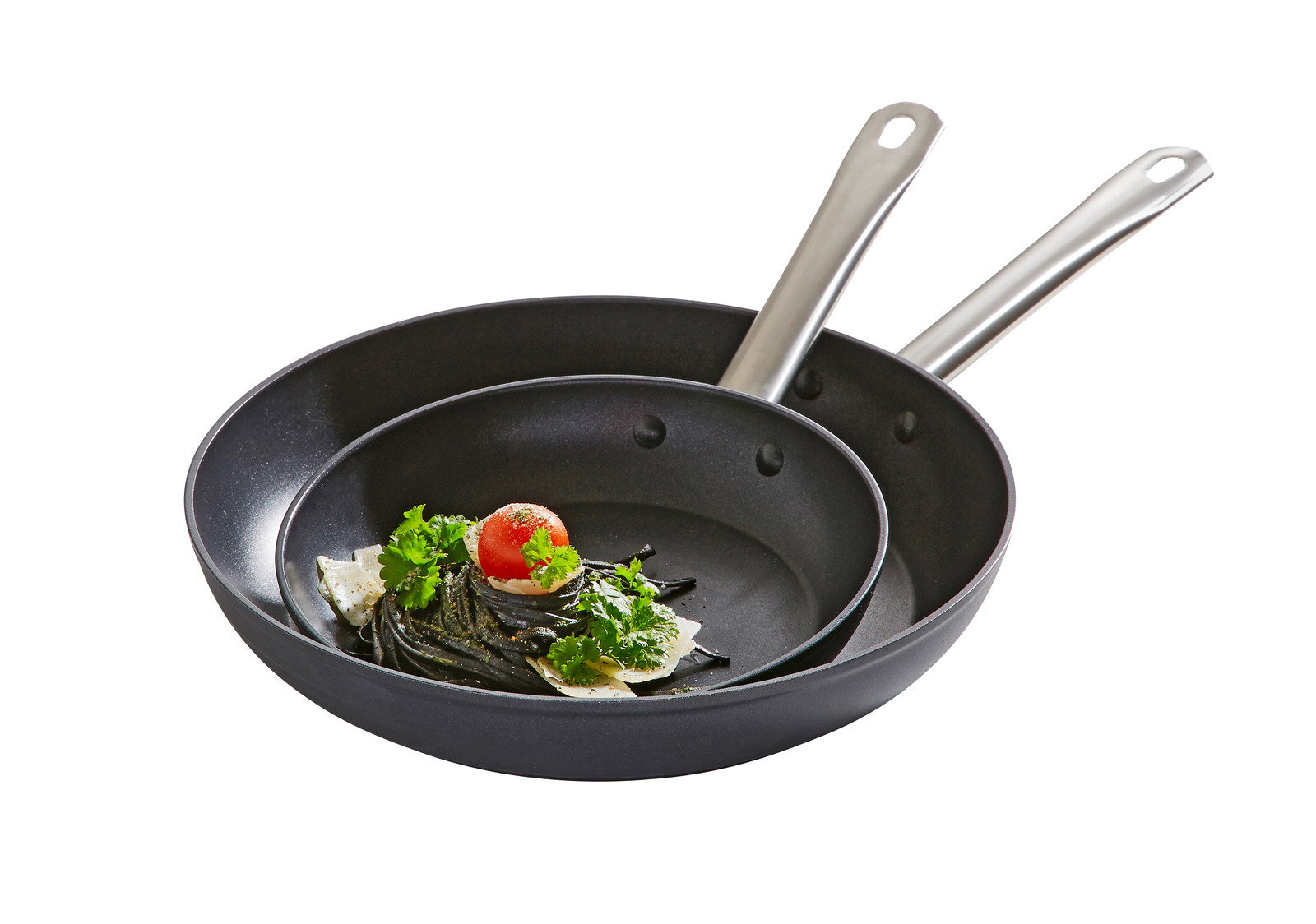 Zwei schwarze Pfannen mit Edelstahlgriffen, ineinander gestapelt, mit einer Portion Pasta und einer Kirschtomate in der kleineren Pfanne, seitliche Perspektive.
