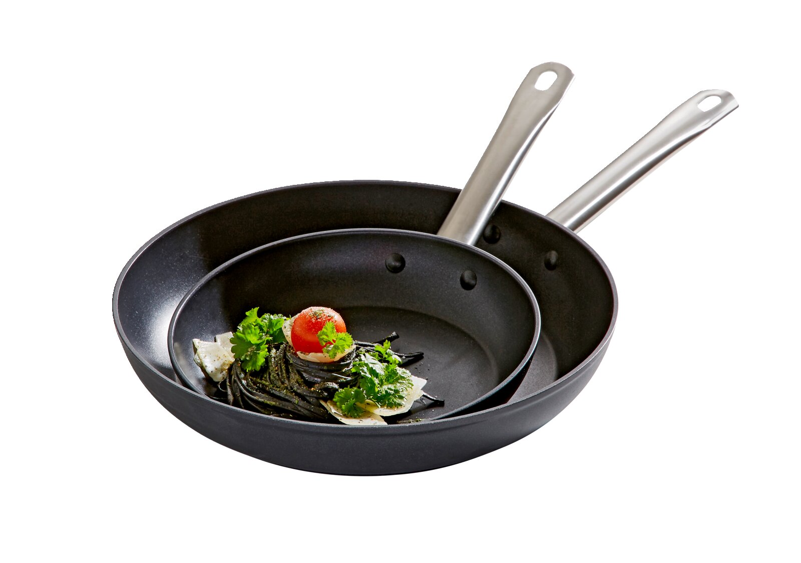 Zwei schwarze Pfannen mit Edelstahlgriffen, ineinander gestapelt, mit einer Portion Pasta und einer Kirschtomate in der kleineren Pfanne, seitliche Perspektive.