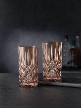 Zwei elegante Longdrinkgläser im Noblesse-Design, aus Kristallglas mit facettiertem Muster, auf einer dunklen Oberfläche stehend, seitliche Perspektive.