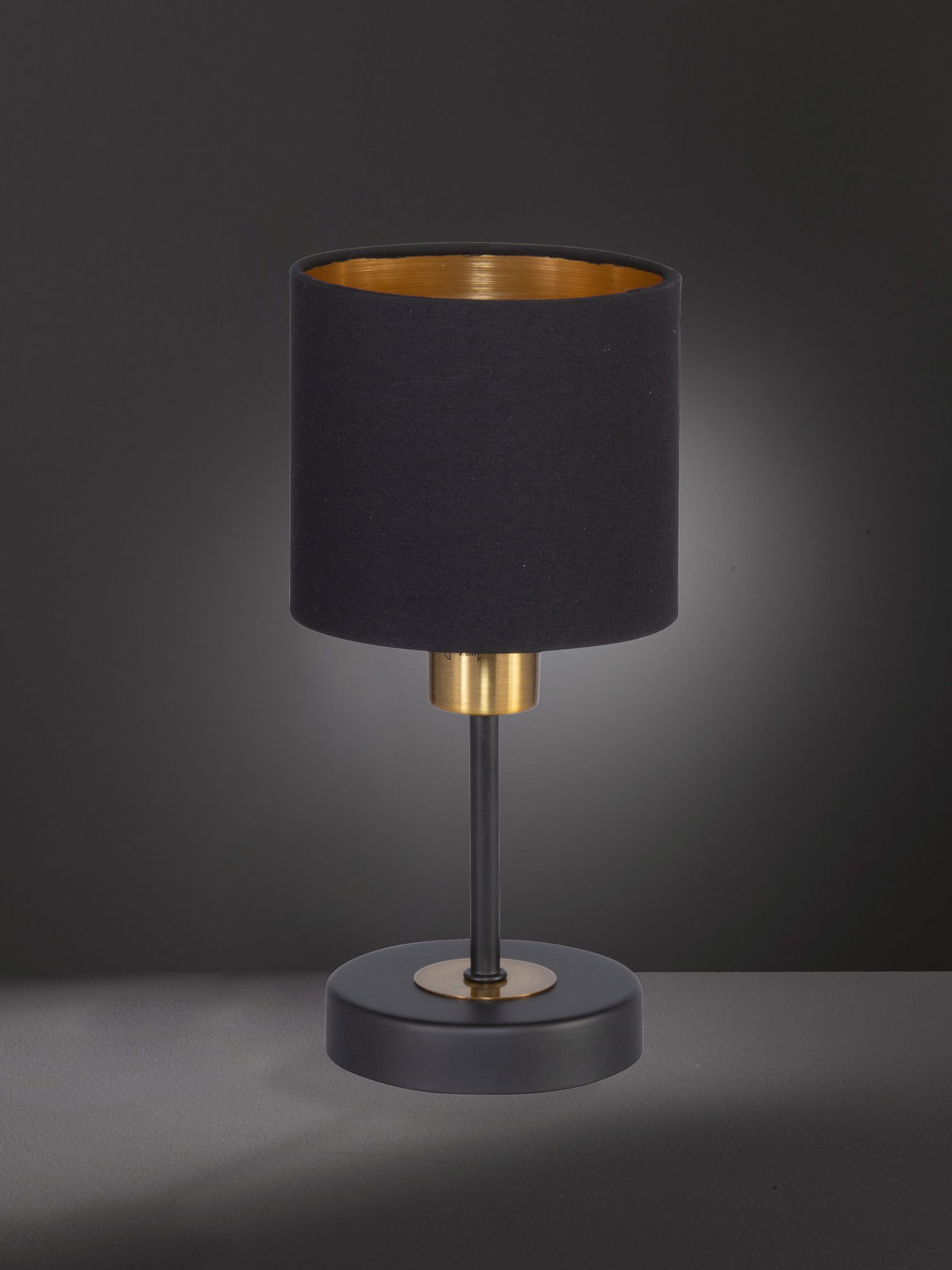 Elegante Tischleuchte mit schwarzem Lampenschirm und goldener Innenseite, frontal betrachtet.