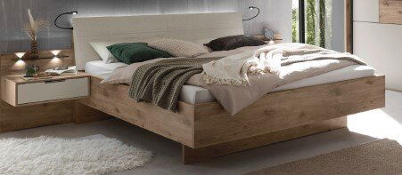 Modernes Holzbett mit gepolstertem Kopfteil in hellem Stoff, weißer Bettwäsche und Decken in Grün und Grau, im Schlafzimmer neben schwebendem Nachttisch – Perspektive: frontale 3/4-Ansicht von schräg vorne.