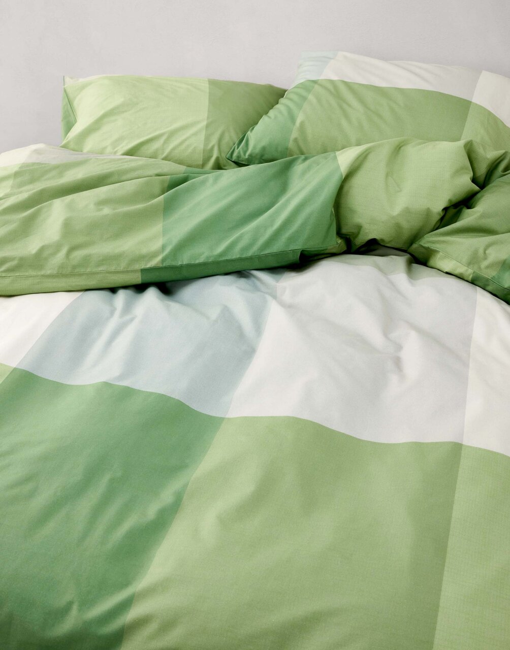 Grüne und weiße Bettwäsche mit Karomuster, aus der Vogelperspektive fotografiert.