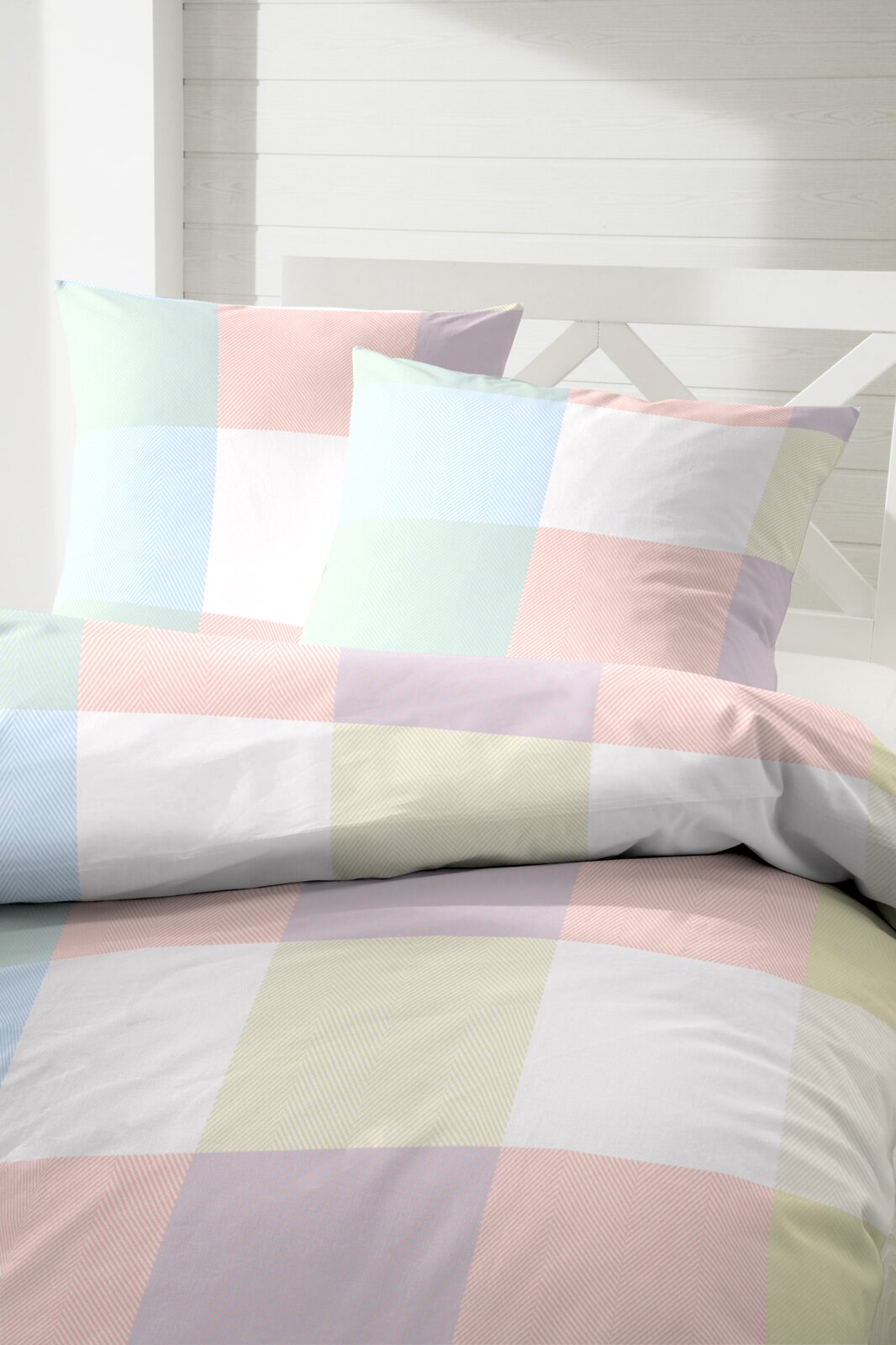 Primera Renforcé Bettwäsche 135/200cm Bettwäsche mit großem Karomuster in Pastellfarben (Hellblau, Rosa, Gelb) und feiner Fischgrät-Struktur, frontal in leichter Schrägansicht auf dem Bett fotografiert
