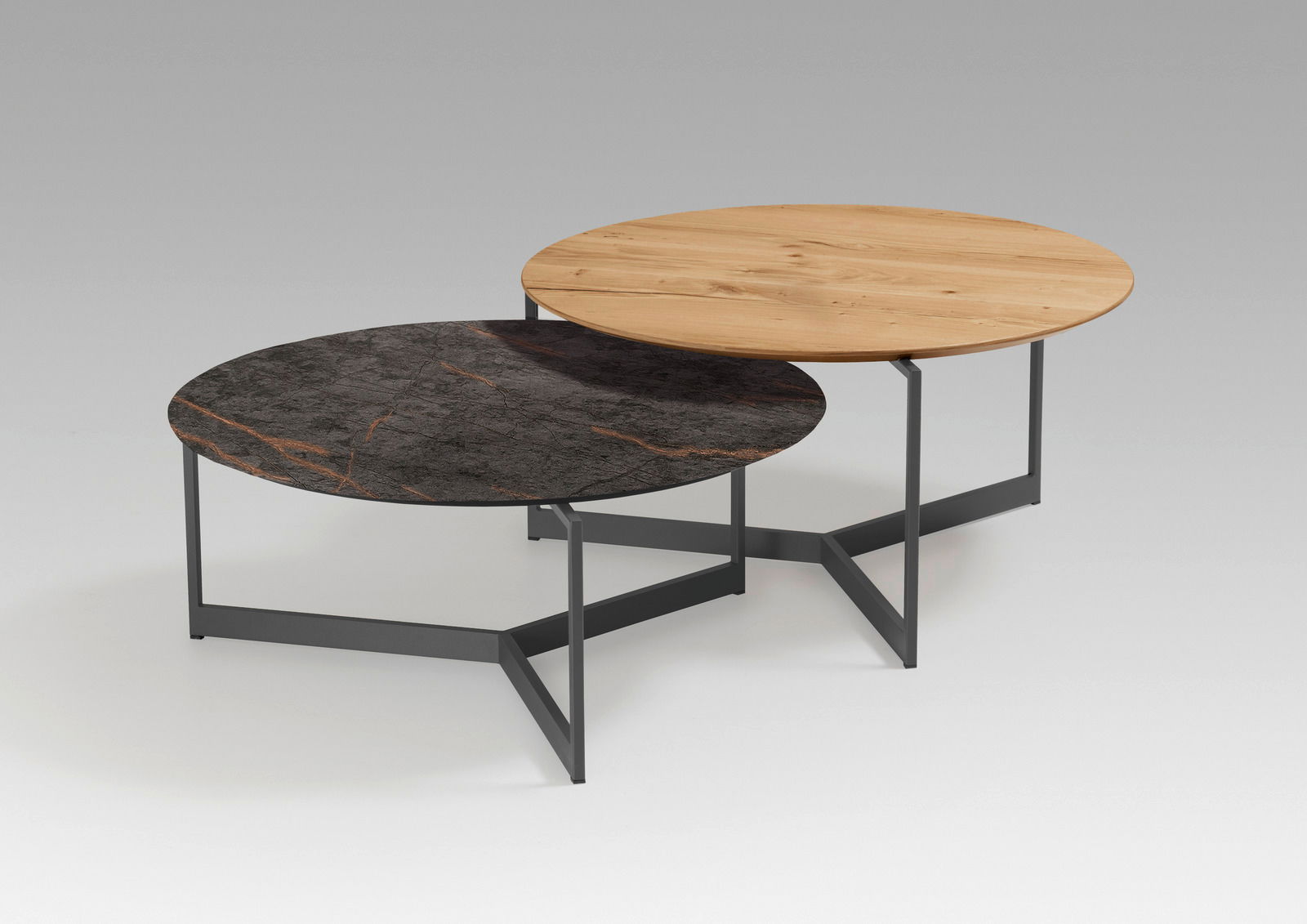 Zwei runde Couchtische mit unterschiedlichen Tischplatten, eine aus Holz und eine aus dunklem Marmor, auf einem modernen Metallgestell. Perspektive von schräg oben.