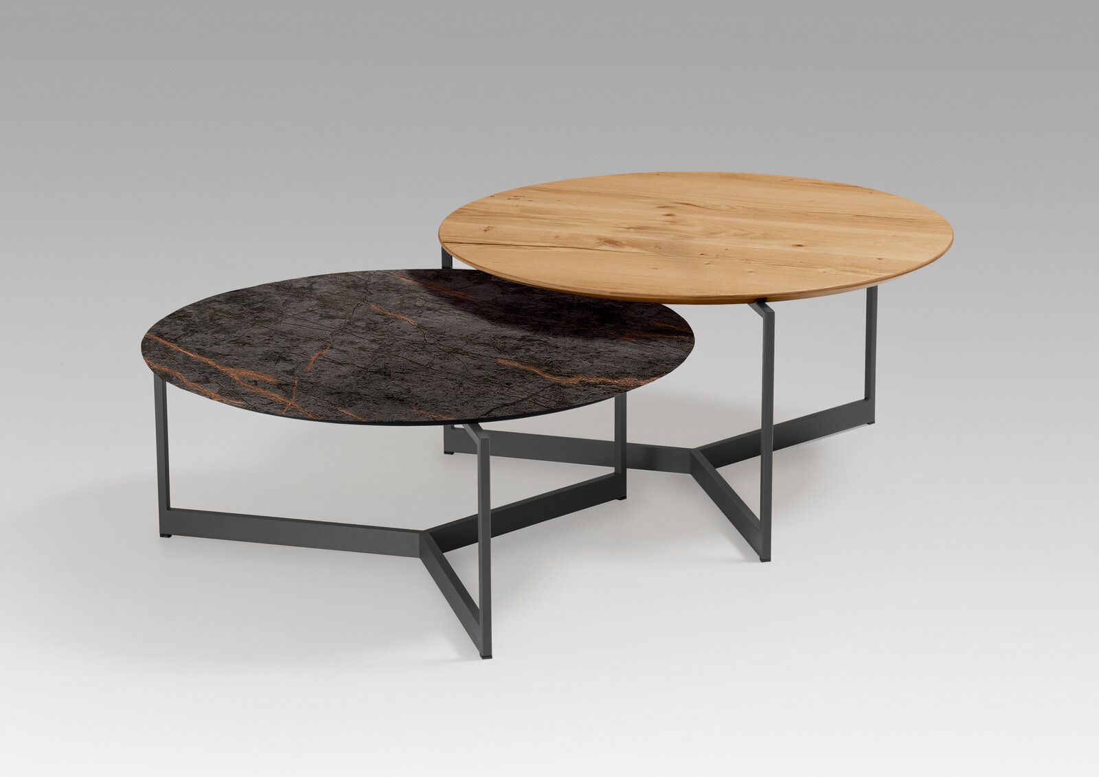 Zwei runde Couchtische mit unterschiedlichen Tischplatten, eine aus Holz und eine aus dunklem Marmor, auf einem modernen Metallgestell. Perspektive von schräg oben.