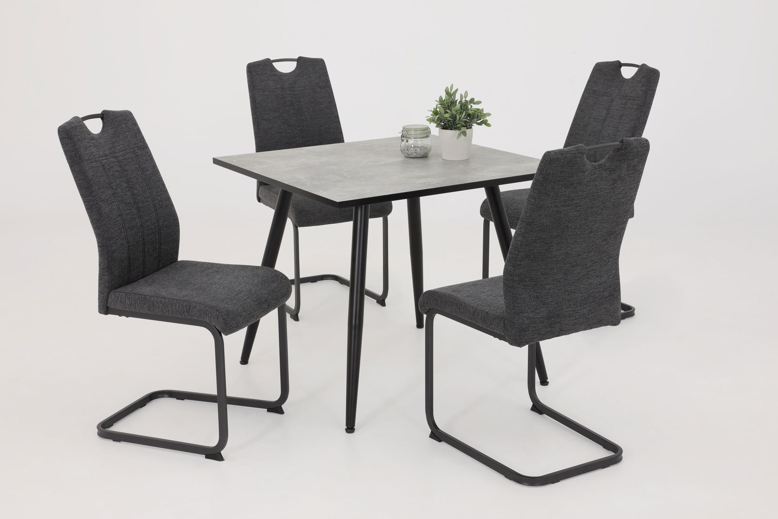 Vier graue Schwingstühle um einen quadratischen Tisch mit schwarzem Gestell, seitliche Perspektive.