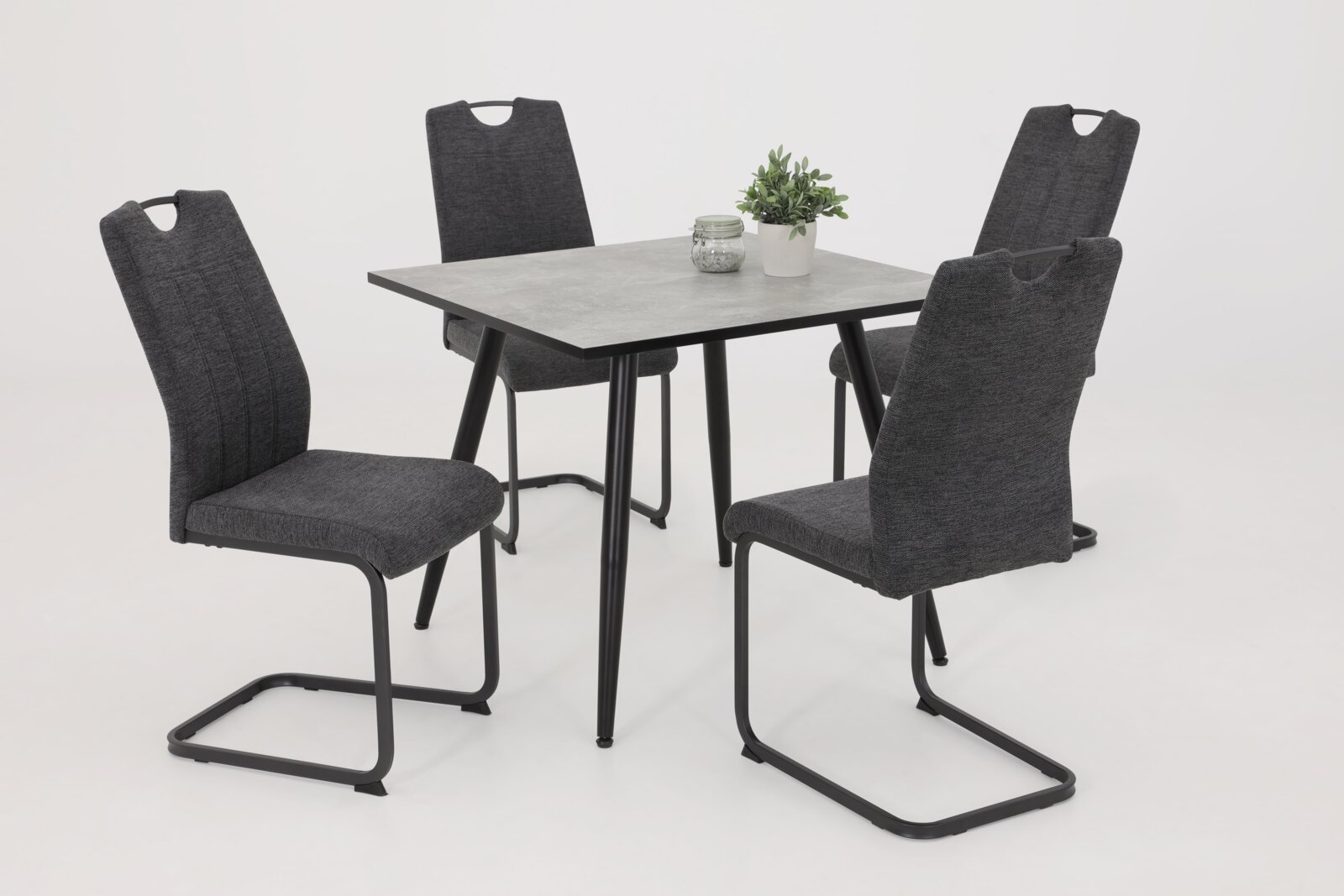 Vier graue Schwingstühle um einen quadratischen Tisch mit schwarzem Gestell, seitliche Perspektive.