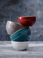 Vier stapelbare Schüsseln in verschiedenen Farben, von oben nach unten: rot, grau, blau und weiß, mit der Aufschrift 'STAUB', seitliche Perspektive.