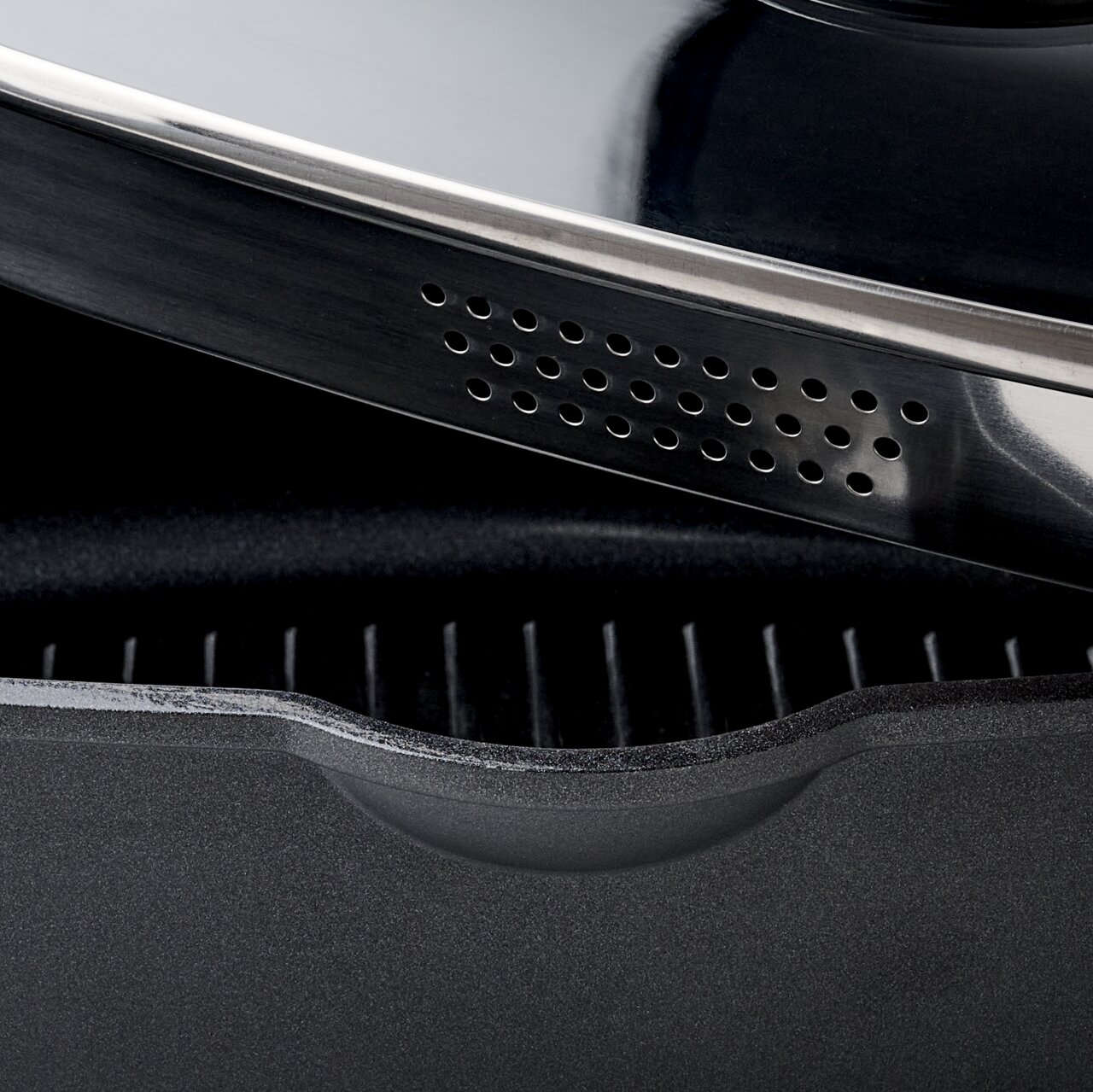 Nahaufnahme eines quadratischen Alugussbräters mit geriffelter Innenfläche und einem Deckel mit Lüftungslöchern.