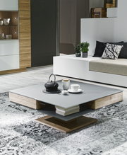 Moderner Couchtisch in quadratischer Form mit grauer Oberfläche und Holzdetails, dekoriert mit Teekanne und Tassen, seitliche Perspektive.