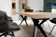Nahaufnahme eines modernen Esstisches mit Holzplatte und schwarzen Metallbeinen, seitliche Perspektive.