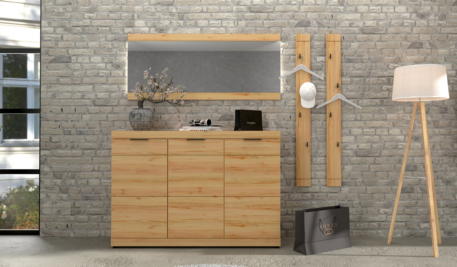 Frontale Ansicht eines modernen Flur-Sets aus hellem Holz mit Sideboard, rechteckigem Wandspiegel, zwei Wandgarderobenleisten mit Kleiderbügeln und Stehlampe vor grauer Ziegelwand.