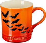 Orange-rote Le-Creuset-Tasse mit schwarzen Fledermausmotiven und cremefarbener Innenseite, in frontaler Seitenansicht leicht von oben