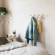 Wandgarderobe mit runden Holzhaken, an der eine Jeansjacke und eine gelbe Tasche hängen, in einem gemütlichen Schlafzimmer mit Pflanzen und einem Nachttisch. Perspektive von der Seite.