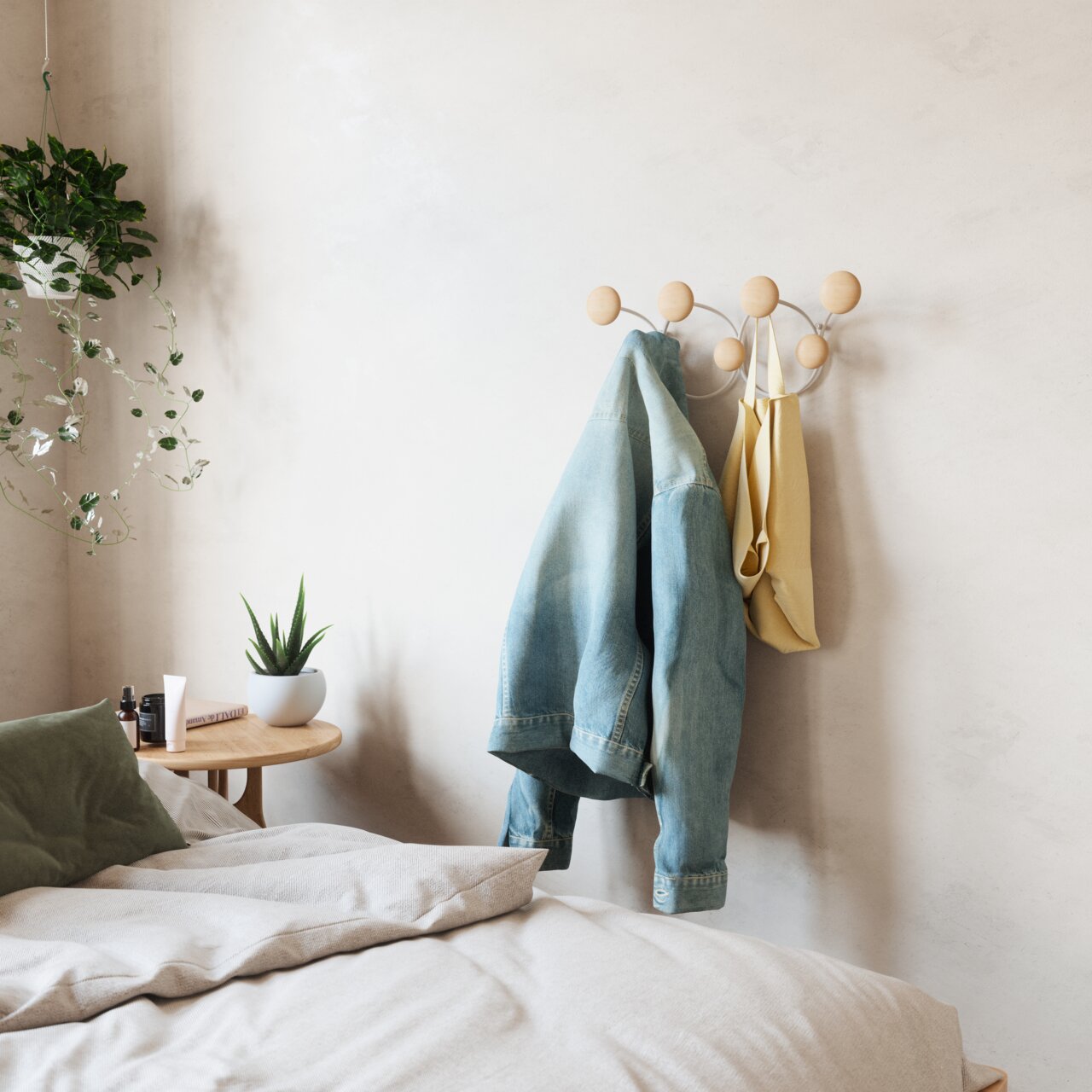 Wandkapstok met ronde houten haken, waaraan een spijkerjasje en een gele tas hangen, in een gezellige slaapkamer met planten en een nachtkastje. Zijaanzicht.