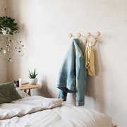 Wandkapstok met ronde houten haken, waaraan een spijkerjasje en een gele tas hangen, in een gezellige slaapkamer met planten en een nachtkastje. Zijaanzicht.