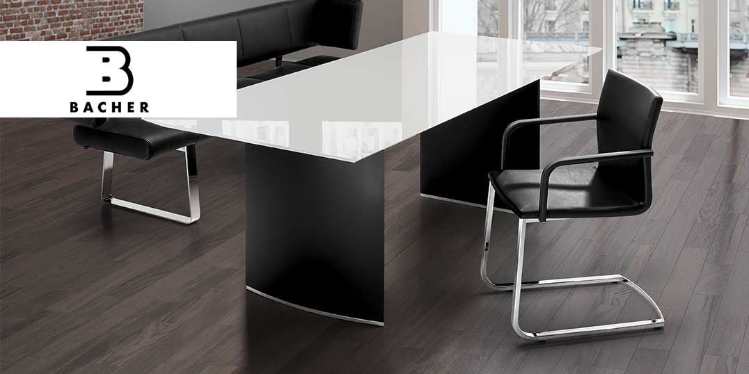 Modernes Bürointerieur mit einem schlichten schwarz-weißen Tischdesign mit Lederstühlen und dem Bacher Logo.