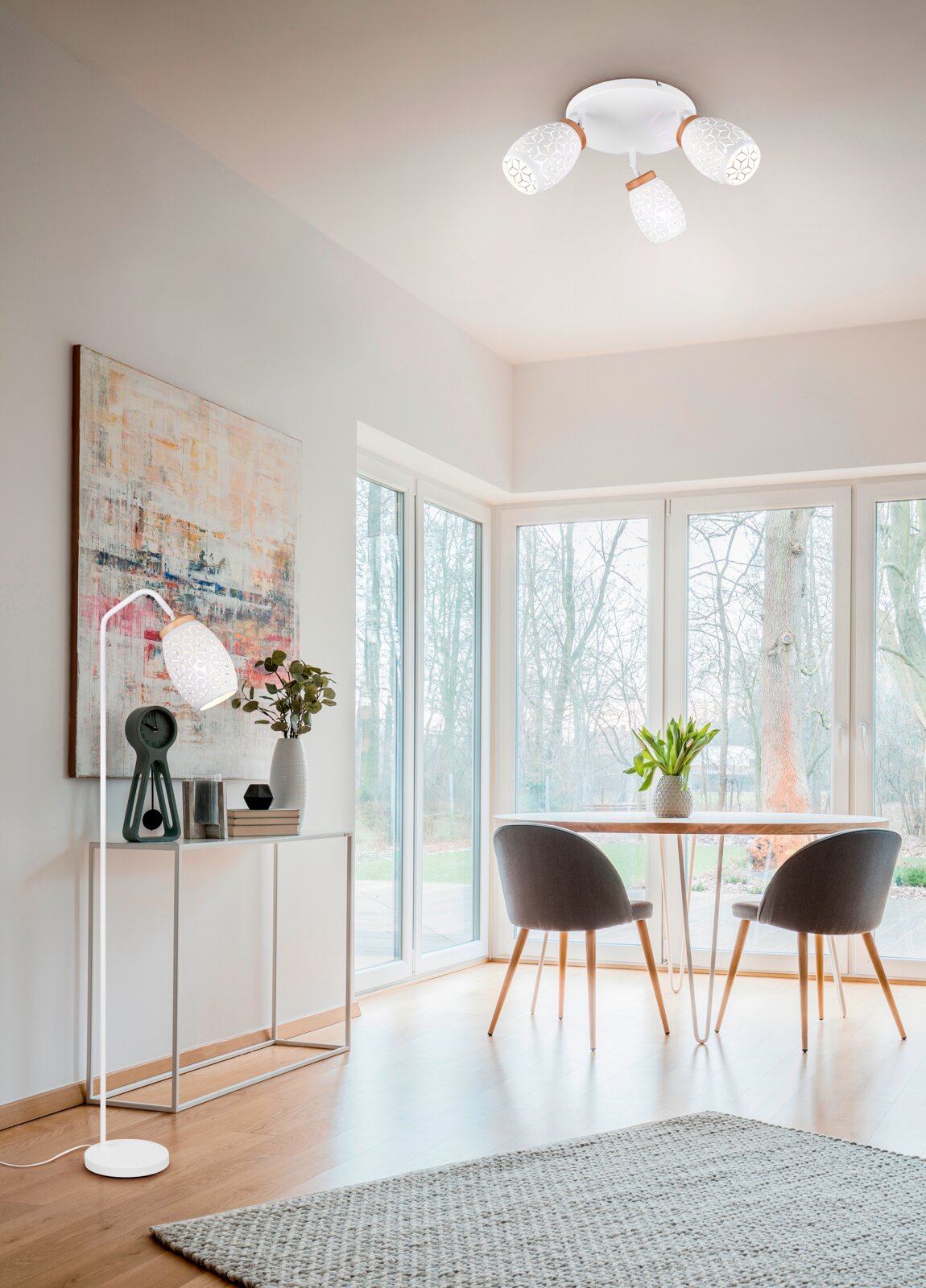 Deckenstrahler mit drei weißen, gemusterten Lampenschirmen in einem modernen Wohnzimmer, seitliche Perspektive.