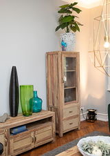 Holzvitrine mit Glastür und zwei Schubladen, dekoriert mit einer Pflanze auf der Oberseite, aus seitlicher Perspektive fotografiert.