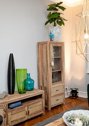 Holzvitrine mit Glastür und zwei Schubladen, dekoriert mit einer Pflanze auf der Oberseite, aus seitlicher Perspektive fotografiert.