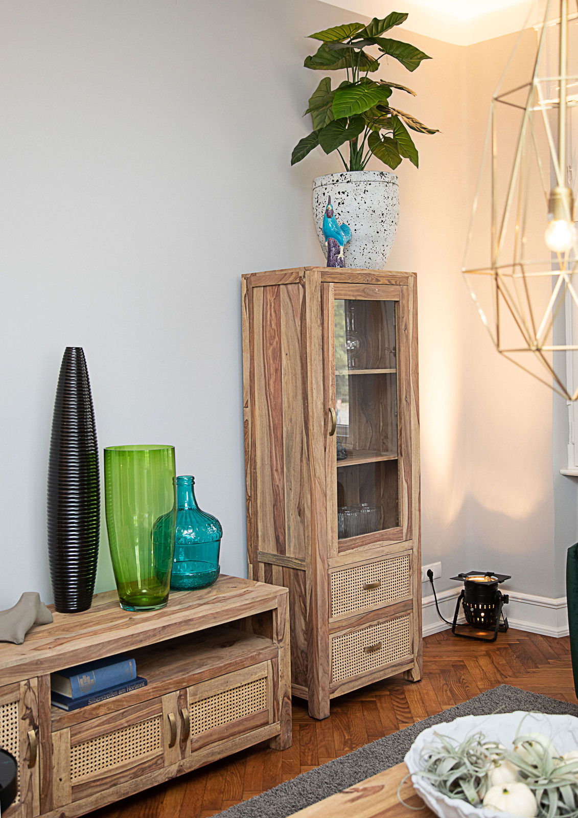 Holzvitrine mit Glastür und zwei Schubladen, dekoriert mit einer Pflanze auf der Oberseite, aus seitlicher Perspektive fotografiert.