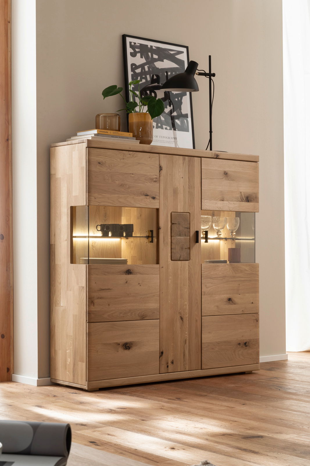 Hochwertiges Highboard aus Holz mit Glaseinsätzen, dekoriert mit Pflanzen und einer Lampe, seitliche Perspektive