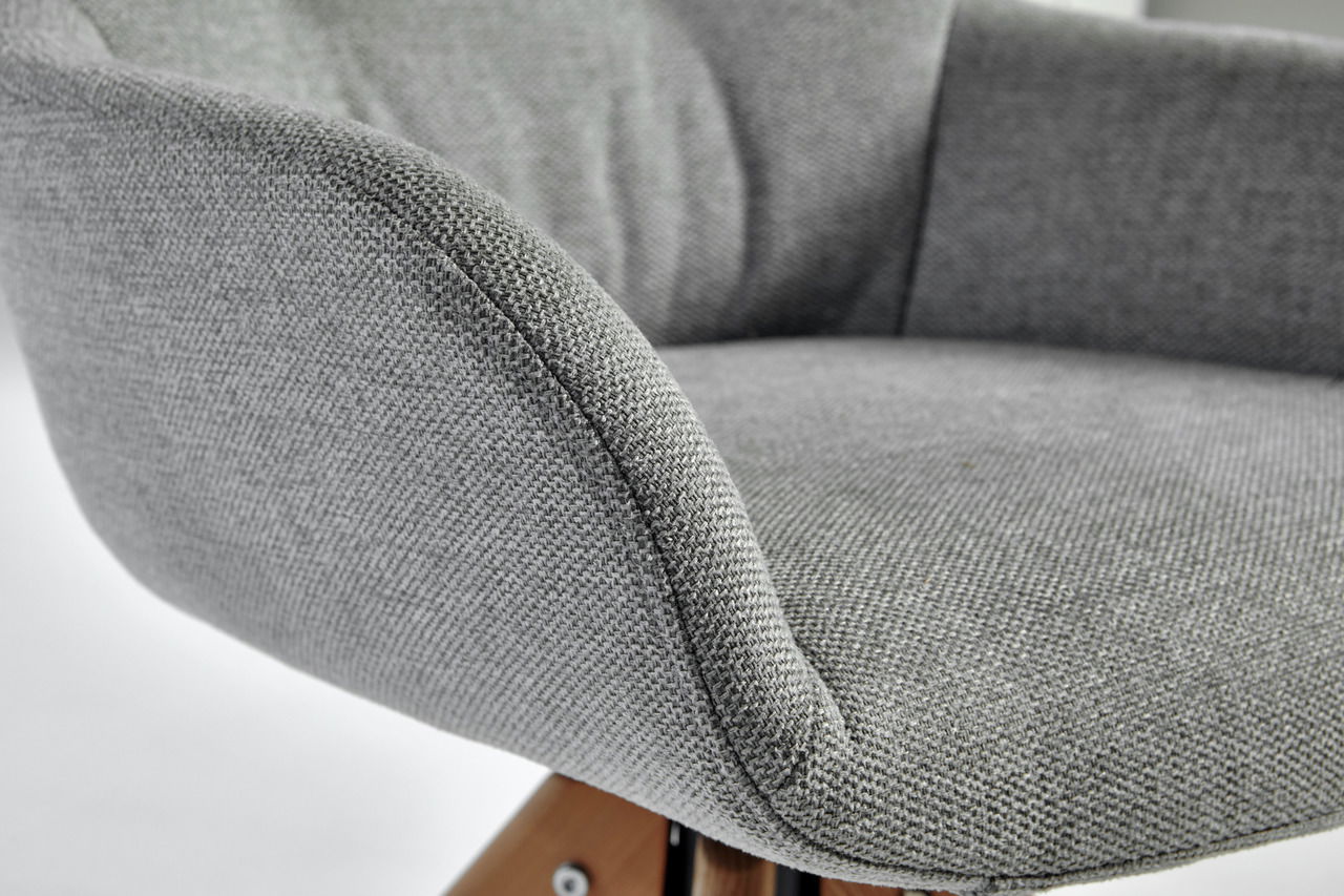 Nahaufnahme eines grauen, gepolsterten Stuhls mit Holzbeinen, seitliche Perspektive