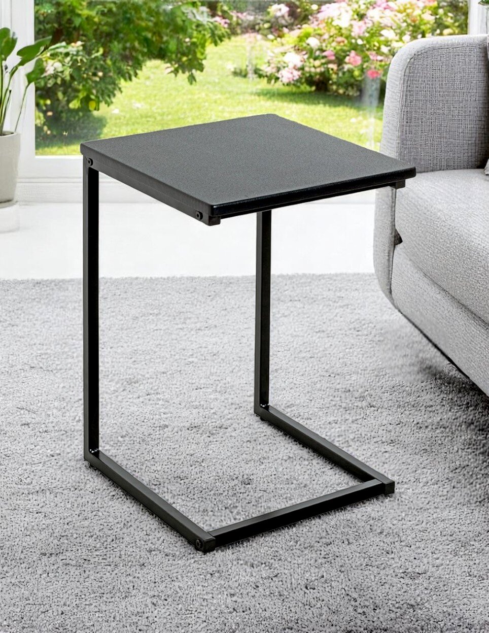 Schwarzer C-förmiger Beistelltisch aus Metall neben einem grauen Sofa auf Teppich, seitliche Perspektive leicht von oben