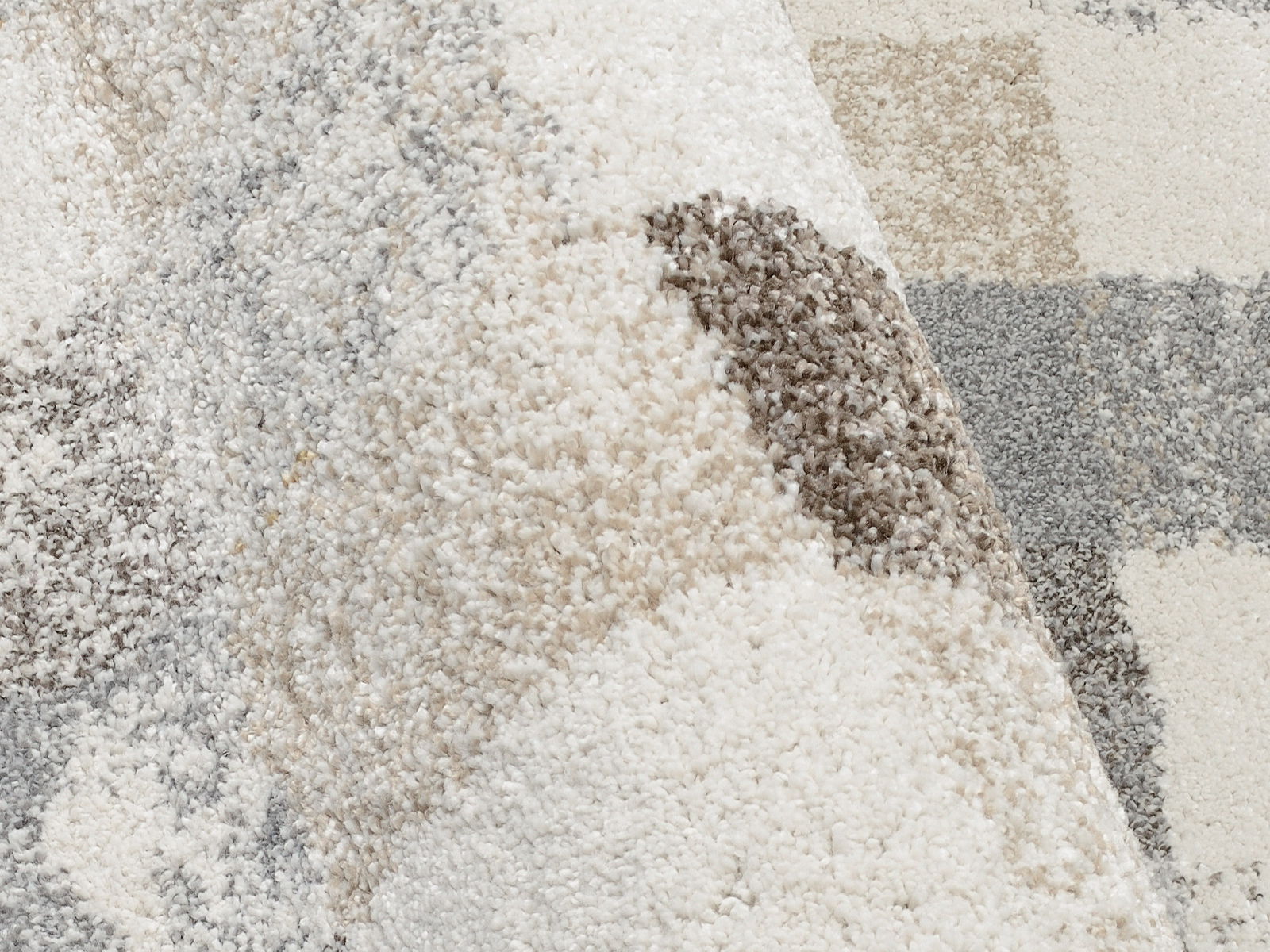 Nahaufnahme eines Frisé-Teppichs mit einem Muster in Beige-, Grau- und Cremetönen, aus einer schrägen Perspektive fotografiert.