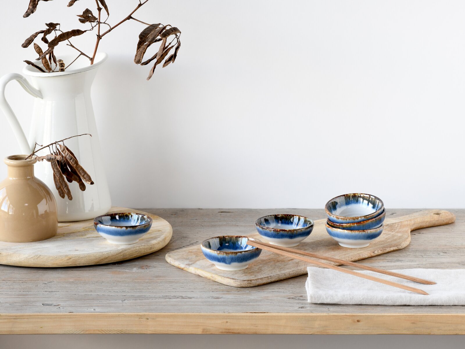 Blau-weiß glasierte Keramikschalen auf Holzbrett mit Essstäbchen und Stoffserviette auf rustikalem Holztisch, perspektivisch in leichter Schrägansicht von vorne.