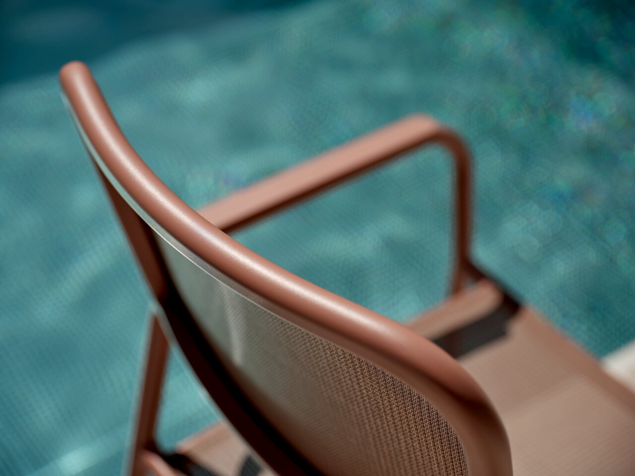 Rückansicht eines braunen Stapelsessels am Pool, Fokus auf die geschwungene Rückenlehne.