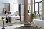 Modernes Badezimmer mit Waschtisch, beleuchtetem Spiegelschrank und Hochschrank in Betonoptik, freistehender Badewanne und großem Fenster, Perspektive: frontale leicht schräge Raumansicht.