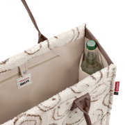 Offene, flauschige Shopper-Tasche in Creme mit braunem Muster und taupefarbenem Innenfutter, Innenfach mit Reißverschluss und Flaschenhalter; Ansicht schräg von oben in den Innenraum