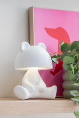 LED Tischlampe in Bärenform auf einem Regal, seitliche Perspektive, neben einer Pflanze und einem pinken Bild.