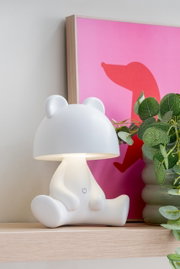 LED Tischlampe in Bärenform auf einem Regal, seitliche Perspektive, neben einer Pflanze und einem pinken Bild.