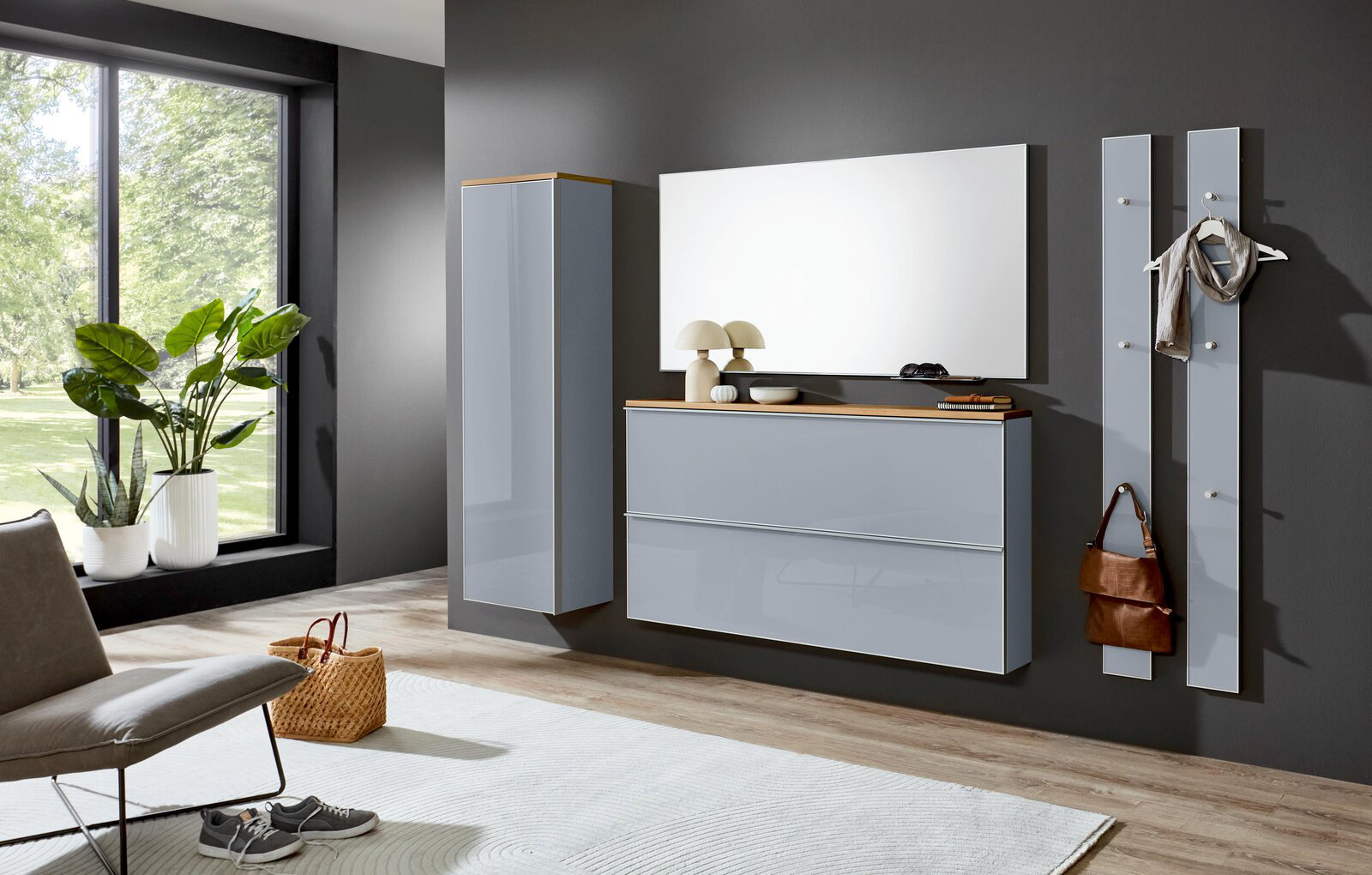 Modernes Flurmöbel-Set in Hellgrau mit Holz-Akzenten: wandhängender Schuhschrank mit zwei Klappen, hoher Hängeschrank, großer Spiegel und zwei Garderobenpaneele an dunkler Wand, gezeigt in frontaler Perspektive mit leichtem Blick von links.