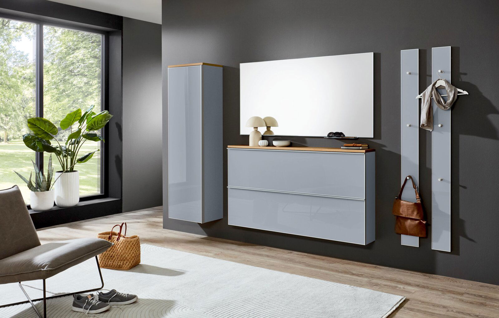 Modernes Flurmöbel-Set in Hellgrau mit Holz-Akzenten: wandhängender Schuhschrank mit zwei Klappen, hoher Hängeschrank, großer Spiegel und zwei Garderobenpaneele an dunkler Wand, gezeigt in frontaler Perspektive mit leichtem Blick von links.