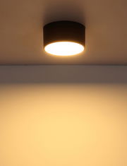 Moderne runde Deckenleuchte in schwarzem Gehäuse, von unten betrachtet, mit warmem Lichtschein an der Decke.