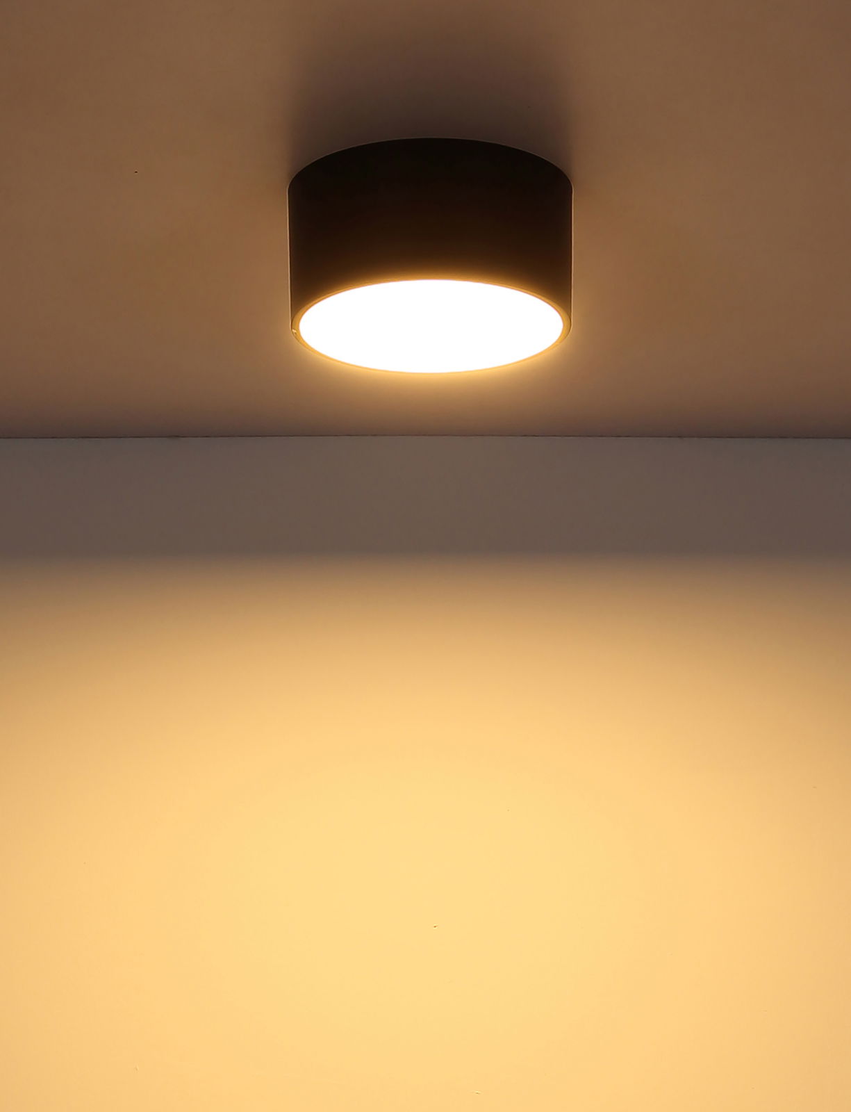 Moderne runde Deckenleuchte in schwarzem Gehäuse, von unten betrachtet, mit warmem Lichtschein an der Decke.